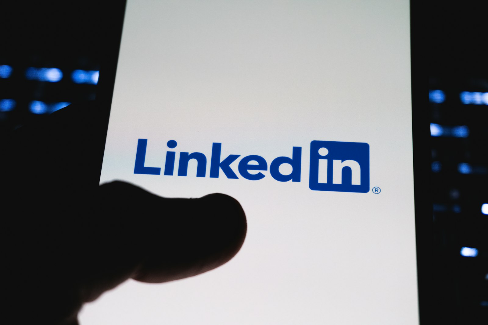 A hand holding a smartphone displaying the LinkedIn logo against a dark background
